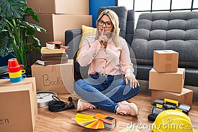 Young hispanic woman moving to a new home sitting on the floor asking to be quiet with finger on lips Stock Photo