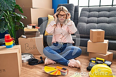 Young hispanic woman moving to a new home sitting on the floor with hand on head, headache because stress Stock Photo