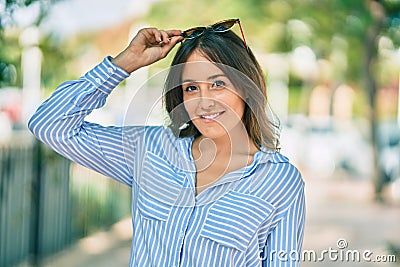 Young hispanic woman smiling happy touching her sunglasses at the park Stock Photo