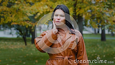 Young hispanic woman standing outdoors feeling toothache holding hand on cheek jaw has dental problems suffering from Stock Photo