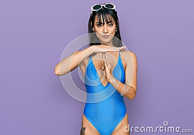 Young hispanic woman wearing swimsuit and sunglasses doing time out gesture with hands, frustrated and serious face Stock Photo