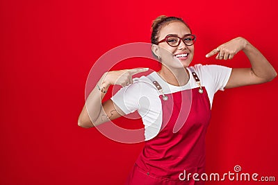 Young hispanic woman wearing waitress apron over red background smiling cheerful showing and pointing with fingers teeth and mouth Stock Photo