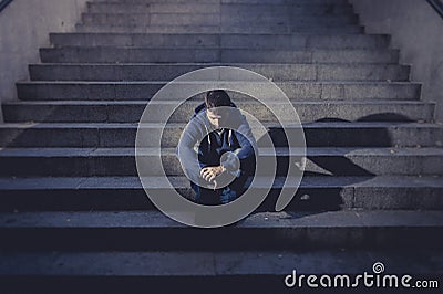 Young homeless man lost in depression sitting on ground street concrete stairs Stock Photo