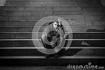 Young homeless man lost in depression sitting on ground street concrete stairs Stock Photo