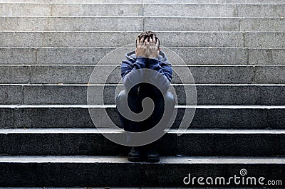 Young homeless man lost job sitting in depression on ground street concrete stairs Stock Photo