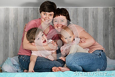 A young homosexual lesbian couple with two children at home, on the bed. Stock Photo