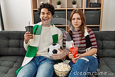 Young hooligan couple supporting soccer team sitting on the sofa at home Stock Photo