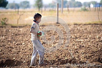 Young indian boy carrying a plastic bottle of water to father working in the field sitting on gunny bag, sacks of wheat Editorial Stock Photo