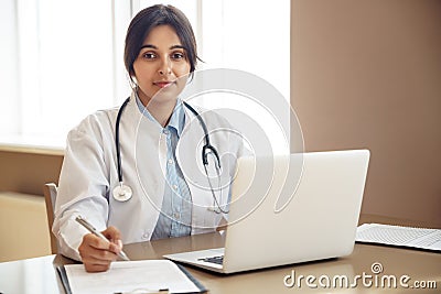 Young indian female doctor wear white coat looking at camera at workplace. Stock Photo