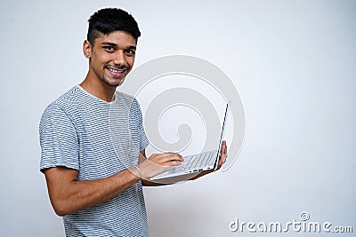 Young Indian handsome boy smiling into the camera while holding his laptop in his arms Stock Photo