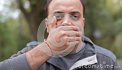 Young Indian man with his hand on his mouth, expression to keep mouth shut Stock Photo