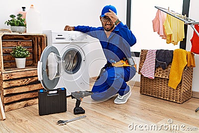 Young indian technician working on washing machine surprised with hand on head for mistake, remember error Stock Photo