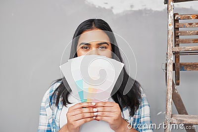 A young Indian woman holds up pale paint swatches to paint repaired wall Stock Photo