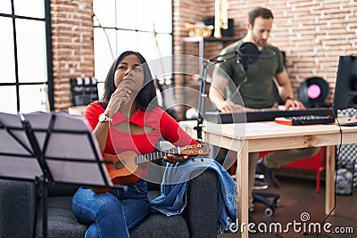 Young indian woman playing ukulele at music studio serious face thinking about question with hand on chin, thoughtful about Stock Photo