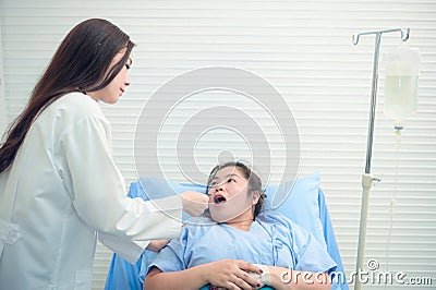 Young inexperienced female doctor taking care of a fat sick woman on the couch in the medical office. Asian doctor and patient Stock Photo