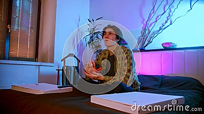 Young interested man sitting on the bed watching TV and eating chips Stock Photo