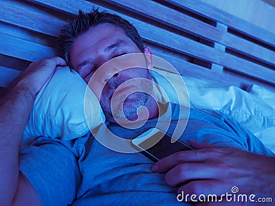 Young internet addict man sleeping on bed holding mobile phone in his hand at night in smartphone and social media network overuse Stock Photo