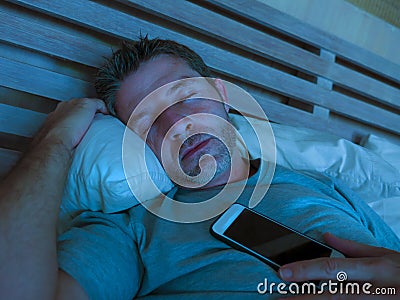 Young internet addict man sleeping on bed holding mobile phone in his hand at night in smartphone and social media network overuse Stock Photo