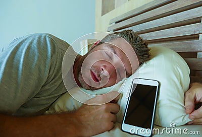 Young internet addict man sleeping on bed holding mobile phone in his hand in smartphone and social media overuse and online addic Stock Photo