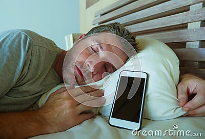 Young internet addict man sleeping on bed holding mobile phone in his hand in smartphone and social media overuse and online addic Stock Photo