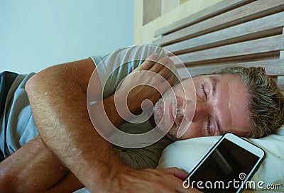 Young internet addict man sleeping on bed holding mobile phone in his hand in smartphone and social media overuse and online addic Stock Photo