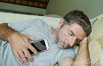 Young internet addict man sleeping on home couch holding mobile phone in his hand in smartphone and social media overuse and onlin Stock Photo