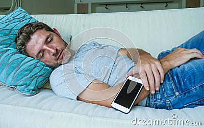 Young internet addict man sleeping on home couch holding mobile phone in his hand in smartphone and social media overuse and onlin Stock Photo