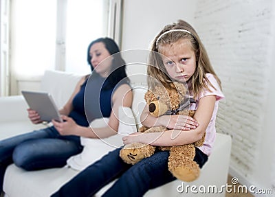 Young internet addict mother using digital tablet pad ignoring little sad daughter Stock Photo