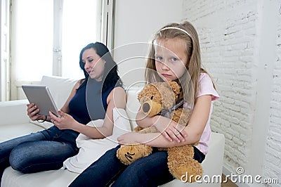 Young internet addict mother using digital tablet pad ignoring little sad daughter Stock Photo