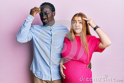 Young interracial couple expecting a baby, touching pregnant belly worried and stressed about a problem with hand on forehead, Stock Photo