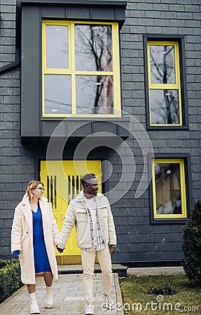 Young interracial couple holds each other hand and walks on street Stock Photo