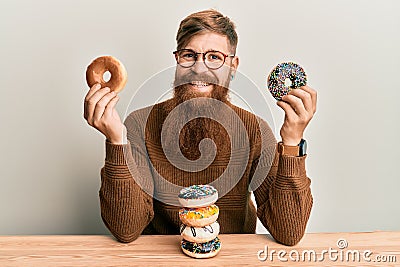 Young irish redhead man eating doughnut for breakfast smiling with a happy and cool smile on face Stock Photo