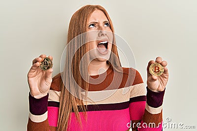 Young irish woman holding virtual currency ethereum coin and bitcoin angry and mad screaming frustrated and furious, shouting with Editorial Stock Photo