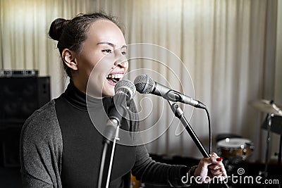 Young Japanese or Caucasian woman singing song loud on two microphones in studio Stock Photo