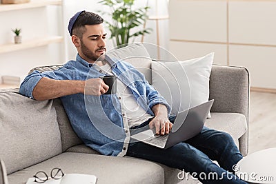 Young jewish man watching video on computer, drinking hot coffee Stock Photo