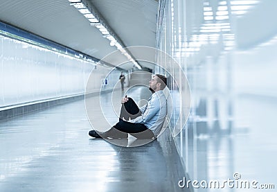 Young jobless business man suffering depression sitting on ground street underground leaning on wall alone looking desperate in Stock Photo