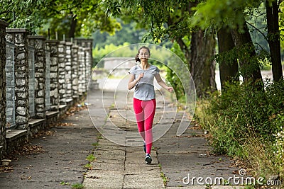 Young jogging woman running through the summer park road. Stock Photo