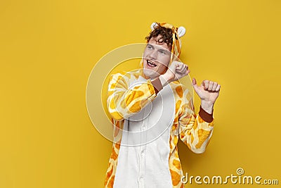 young joyful guy in funny children's giraffe pajamas dances on yellow background, man in animal cosplay clothes Stock Photo