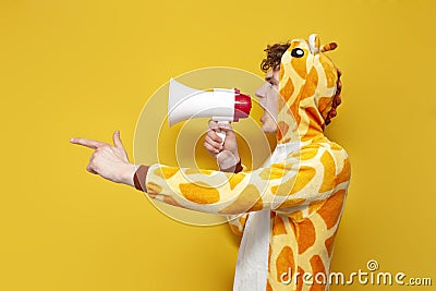 young joyful guy in funny children's giraffe pajamas speaks into megaphone and points his hand to the side Stock Photo