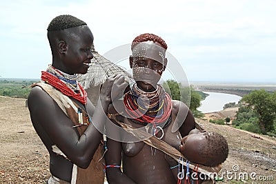 A young karo woman is painting the face of another woman carrying her child in her arms Editorial Stock Photo