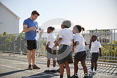 Young kids in a school playground with teacher holding ball Stock Photo