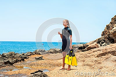 Young lady in diving suit with paddles standing on rock coast. Stock Photo