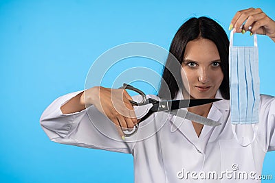 A young lady doctor is holding tailor`s scissors in front of her with a protective mask ready for cutting. The end of Stock Photo