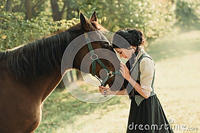 A young lady in a vintage dress, with tenderness and with affection hugs her horse. An ancient, collected hairstyle, a Stock Photo