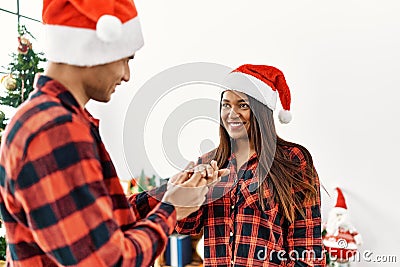 Young latin couple celebrating christmas holding engagement ring for wedding proposal at home Stock Photo