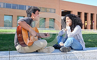 Young latin couple in love playing the guitar and singing at the university campus Stock Photo