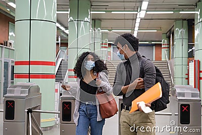 Young latin couple wearing protective face mask walking through subway turnstile at the train or metro station Stock Photo