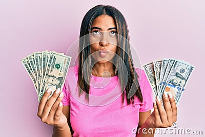 Young latin girl holding dollars making fish face with mouth and squinting eyes, crazy and comical Stock Photo