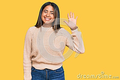 Young latin girl wearing wool winter sweater waiving saying hello happy and smiling, friendly welcome gesture Stock Photo