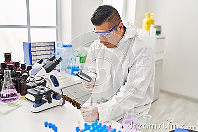 Young latin man scientist looking cannabis herb with loupe at laboratory Stock Photo